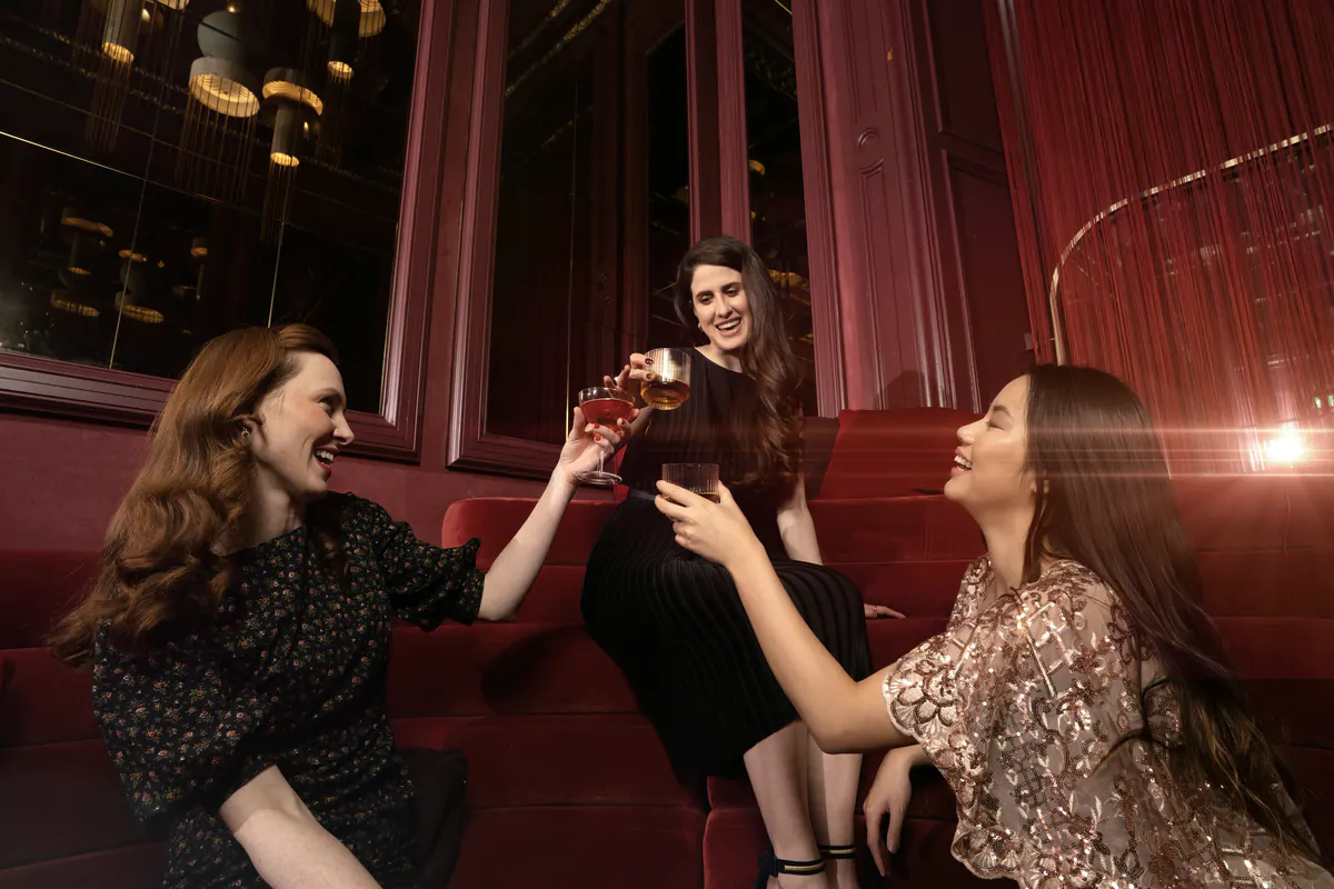 Three friends raising a toast on a burgundy velvet banquette